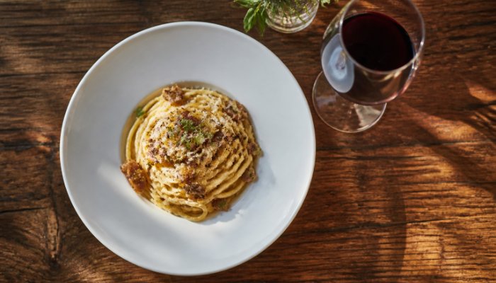An overhead shot of a beautifully plated gourmet pasta dish and a glass of wine on a rustic wooden table, soft evening l