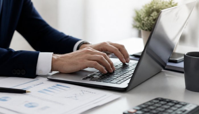 A close-up of a person's hands typing on a sleek laptop with a clean, professional desk setup, focusing on the precision